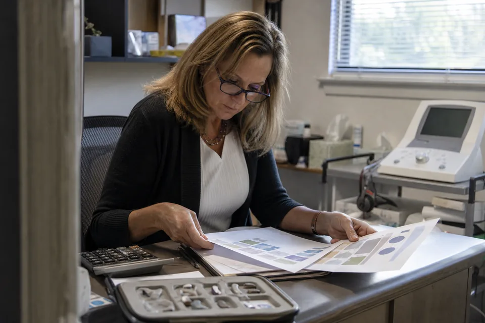 Hearing clinic owner comparing marketing agency proposals with a calculator at her office desk
