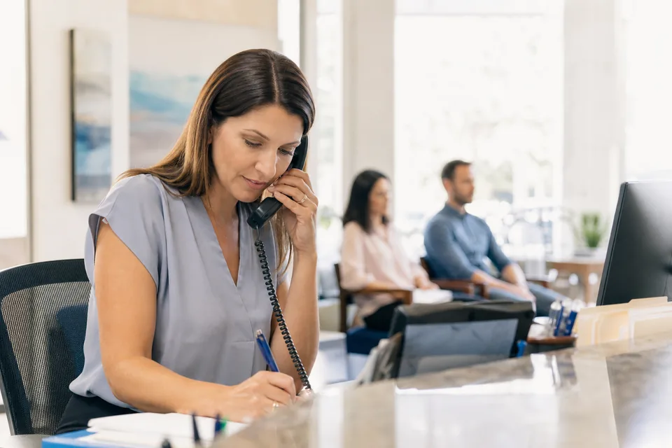 Tax office receptionist answering a new client call at the front counter during filing season