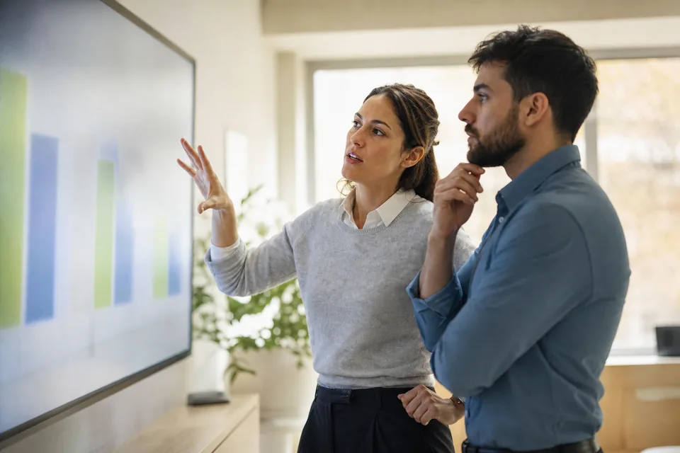 Two colleagues reviewing marketing results on a large wall screen