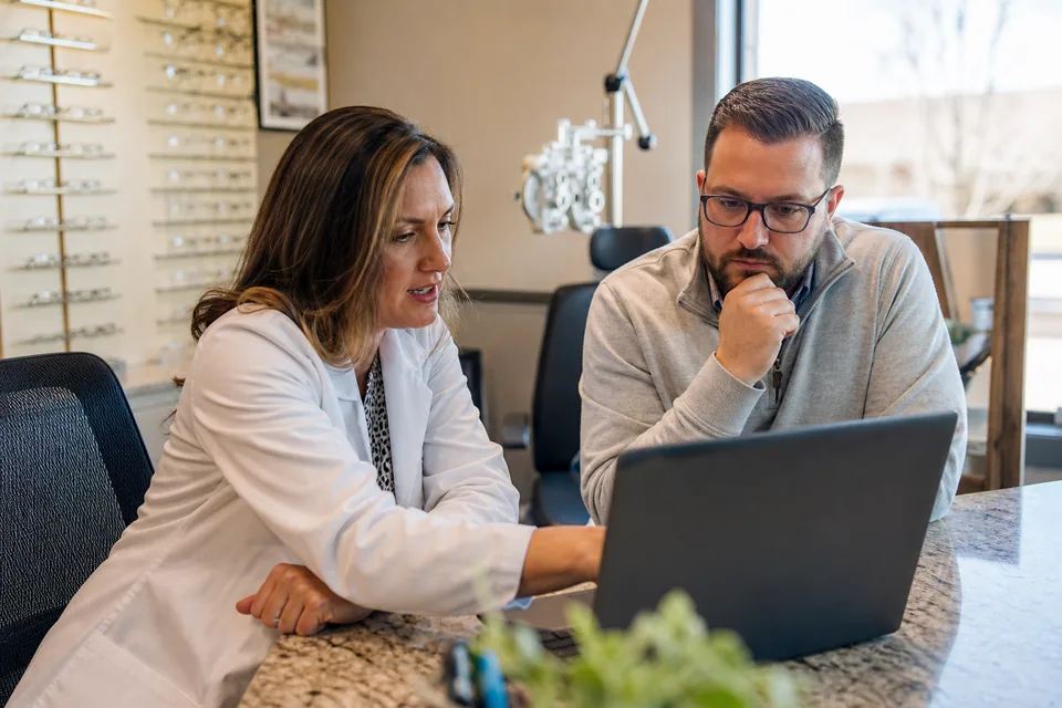 Optometrist and office manager reviewing the practice's marketing on a laptop at the front desk
